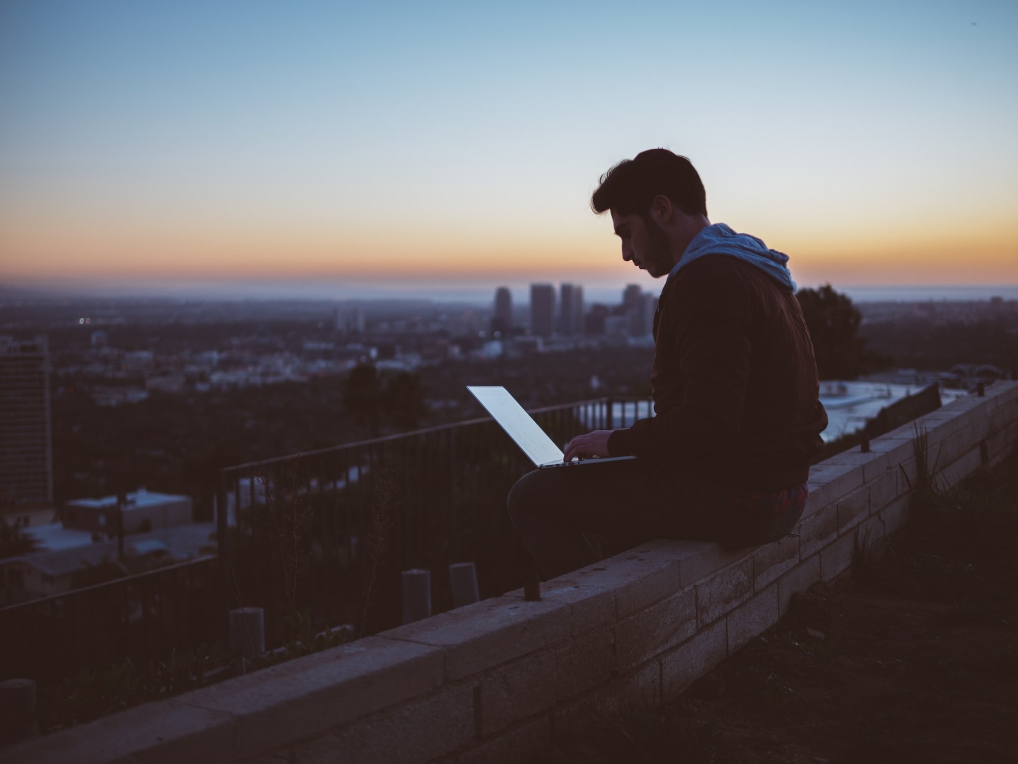 Image of man sitting outside looking at his computer. Image links to webpage describing telehealth services.