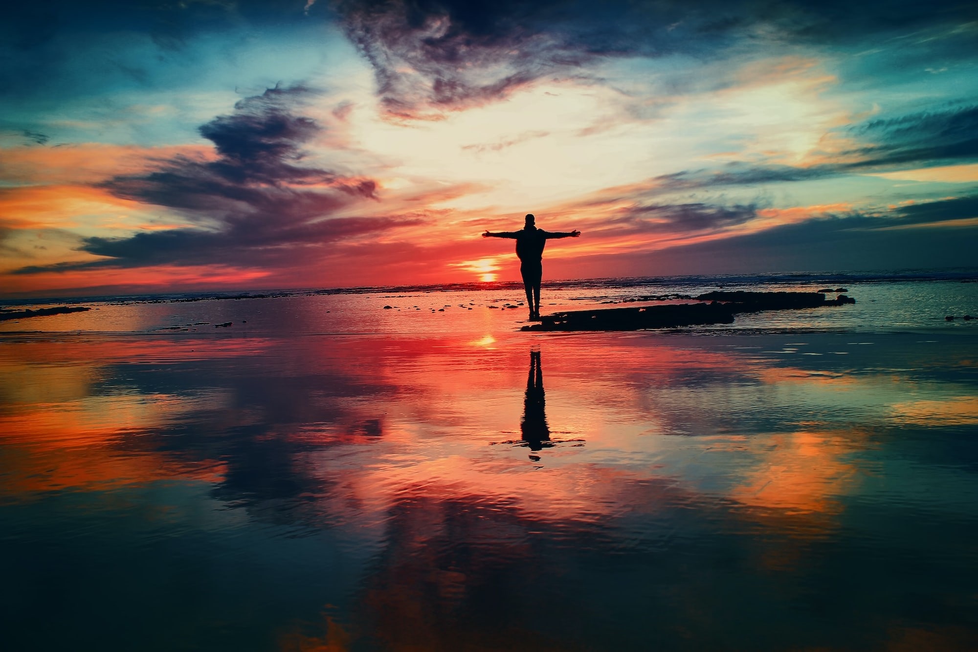 Image of person standing at the ocean with a very colorful sunset around them. The person looks free after healing and overcoming narcissistic abuse.